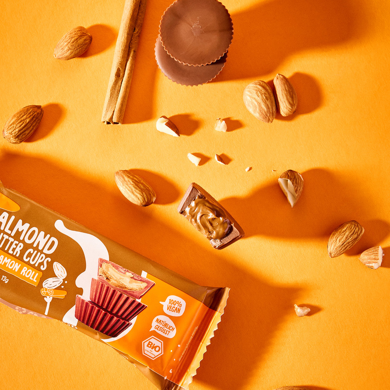 Bio Nutbutter Cups Mixed Box mit Mandeln, Zimtstangen und Schokoladenbechern auf orangefarbenem Hintergrund